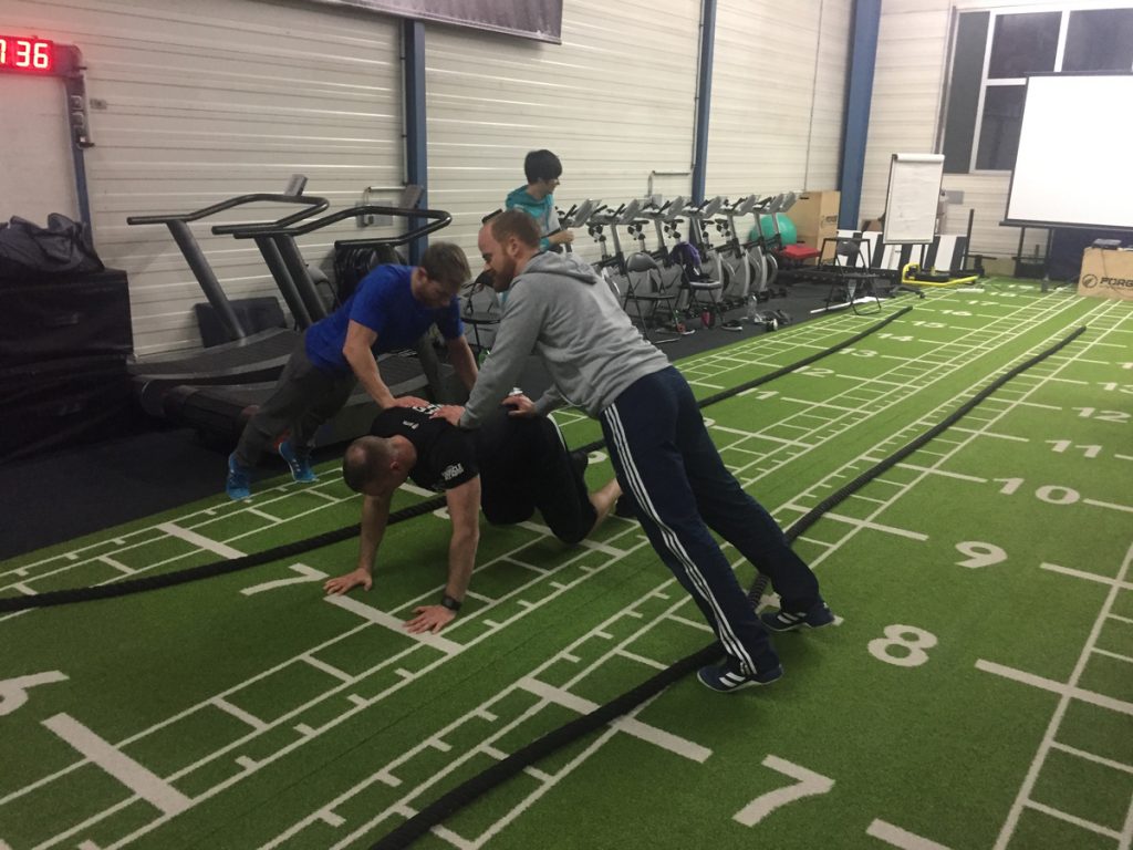 3 Männer beim Training in einer Halle mit grünem Teppich auf dem Zahlen stehen.